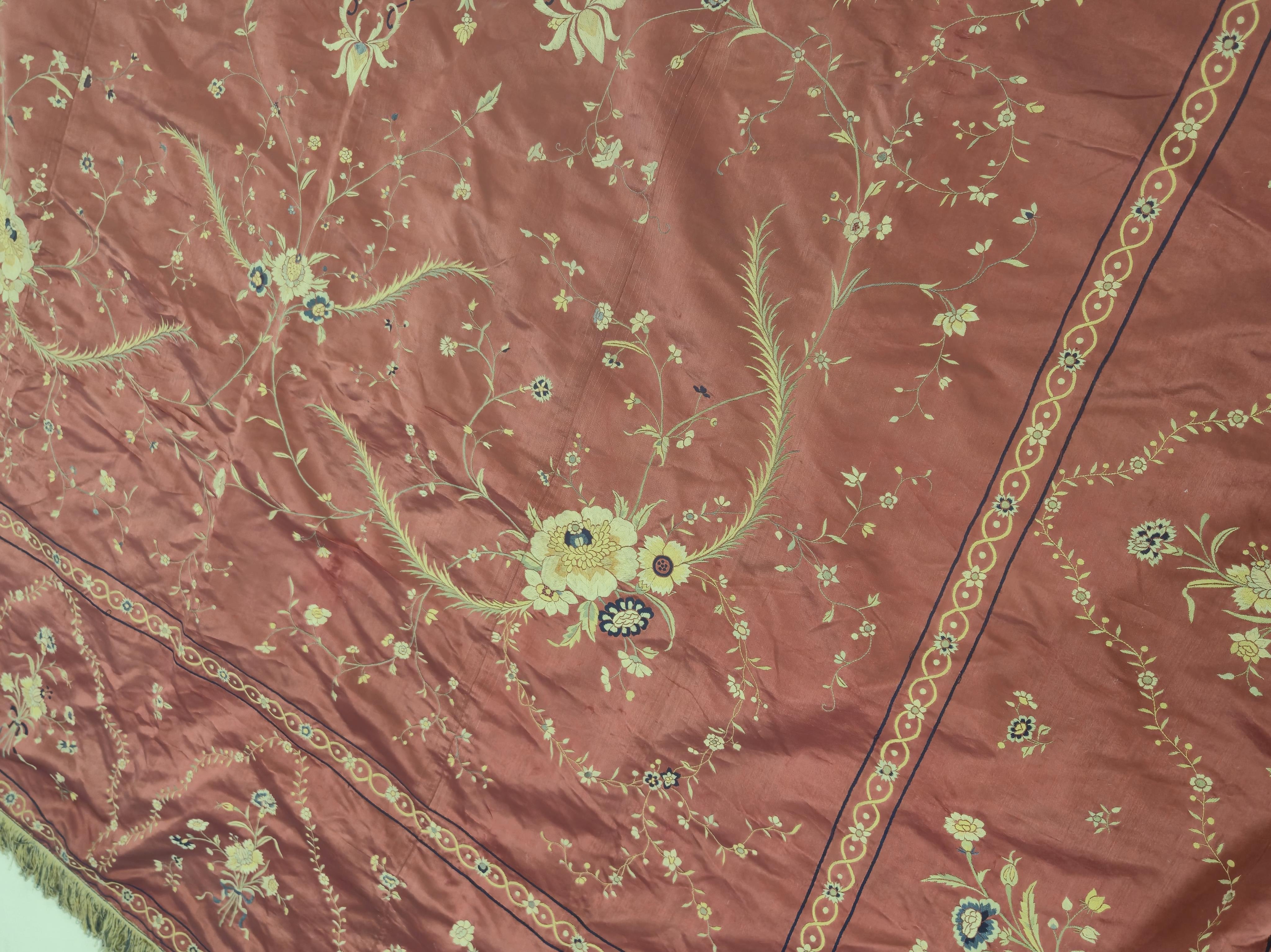 A Chinese 19th century Qing Dynasty crimson red silk embroidered hanging. Embroidered with sprays and swags of flowers and foliage, depicting prosperity and fortune, around a central stylistic sun motif, depicting perfec